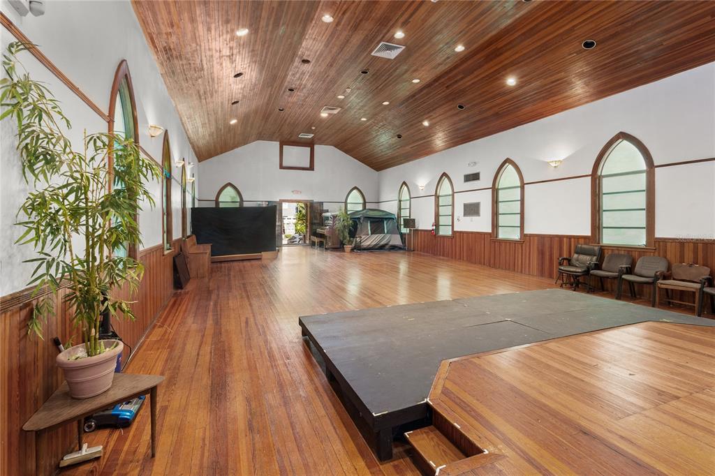 A large hall features a wooden vaulted ceiling, hardwood floors, arched windows, and a stage — 619 NE 1ST STREET, GAINESVILLE, FL