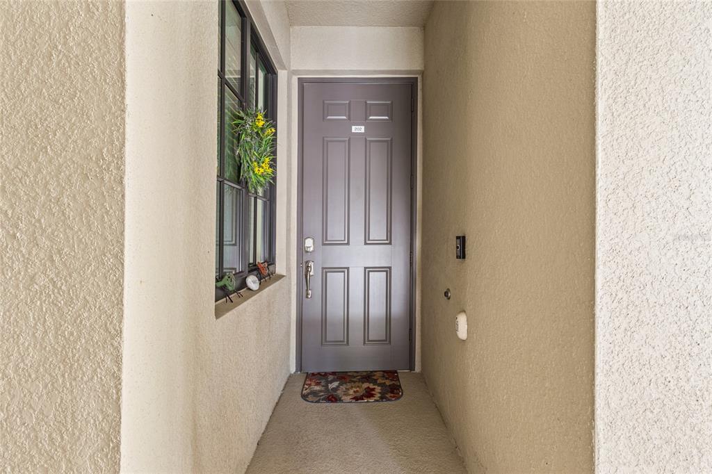 A gray front door with a small wreath sits at the end of a stucco entryway — 17626 GAWTHROP DRIVE UNIT 202, BRADENTON, FL