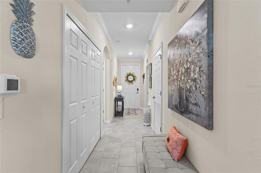 A tiled entryway hallway features a bench, a large floral painting, and a front door — 17626 GAWTHROP DRIVE UNIT 202, BRADENTON, FL