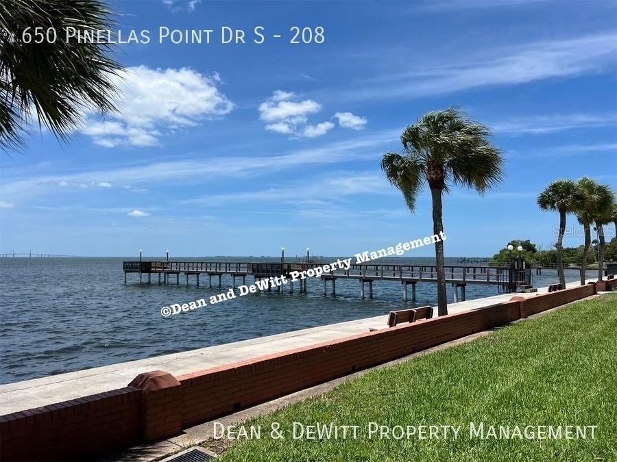 A brick wall borders a grassy lawn overlooking a wooden pier and the open water — 650 PINELLAS POINT DRIVE S UNIT 208, ST PETERSBURG, FL