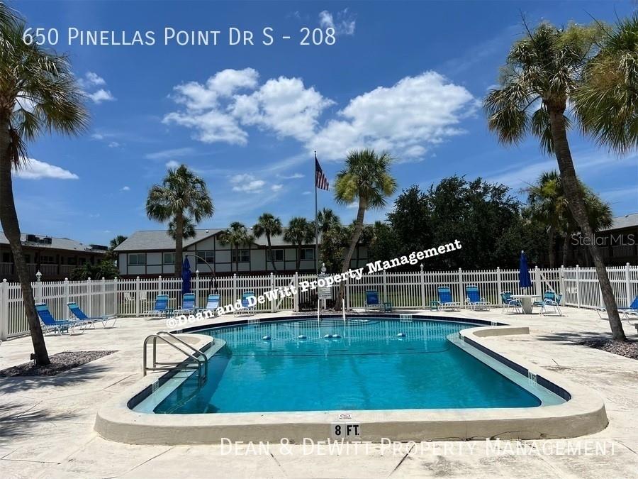 A swimming pool is surrounded by a white fence, lounge chairs, and palm trees — 650 PINELLAS POINT DRIVE S UNIT 208, ST PETERSBURG, FL