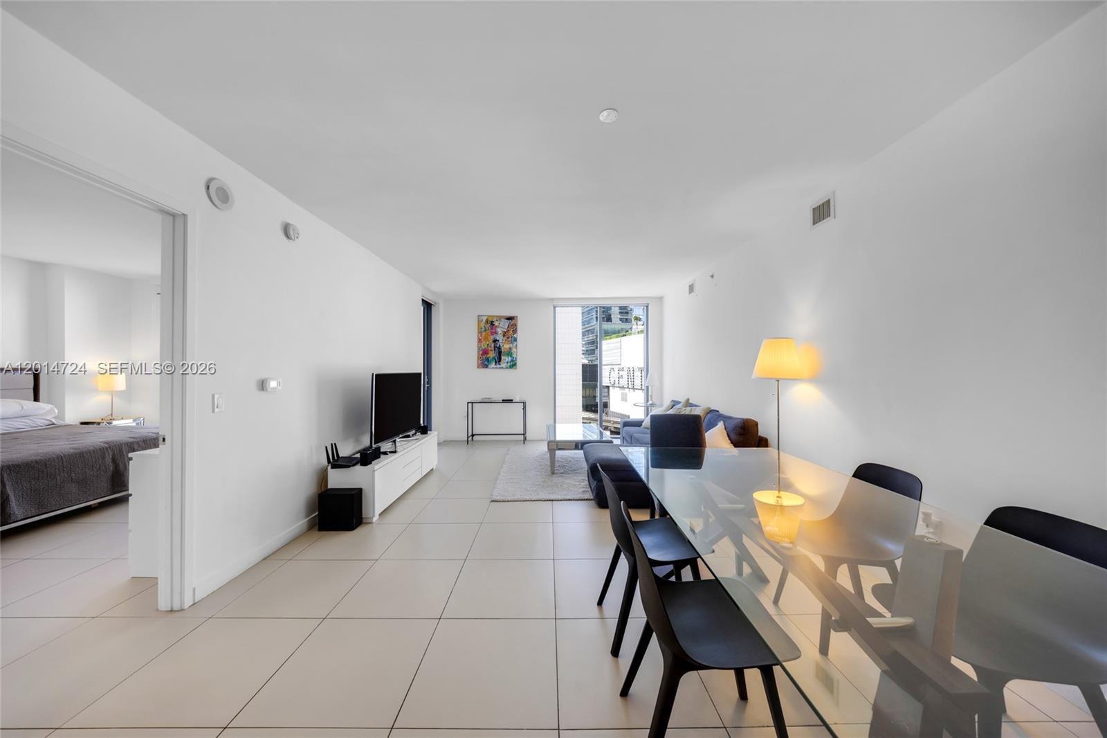 A living and dining area with white tile floors, a glass table, and adjacent bedroom — 31 SE 6th St # 907, Miami FL 33131, MIAMI, FL