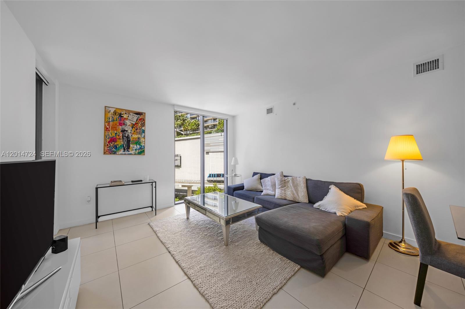 A living room features a gray sectional sofa, a glass coffee table, and tile flooring — 31 SE 6th St # 907, Miami FL 33131, MIAMI, FL
