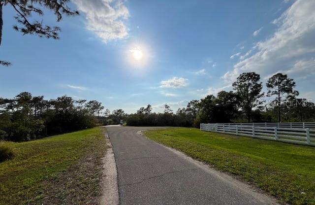 A paved road leads toward a treeline next to a white fence under a sunny sky — 24005 83RD AVENUE E, MYAKKA CITY, FL