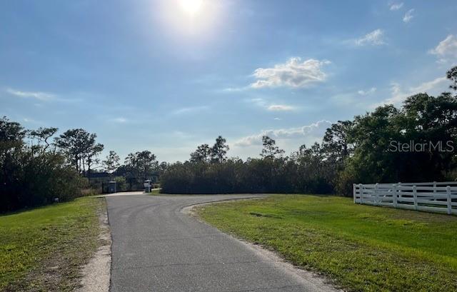 A paved driveway leads toward a gated entrance bordered by a white fence and trees — 24005 83RD AVENUE E, MYAKKA CITY, FL