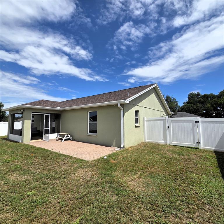 A backyard view of a house with a screened porch, brick patio, and white fence — 2269 COUNTRY MANOR STREET, BARTOW, FL