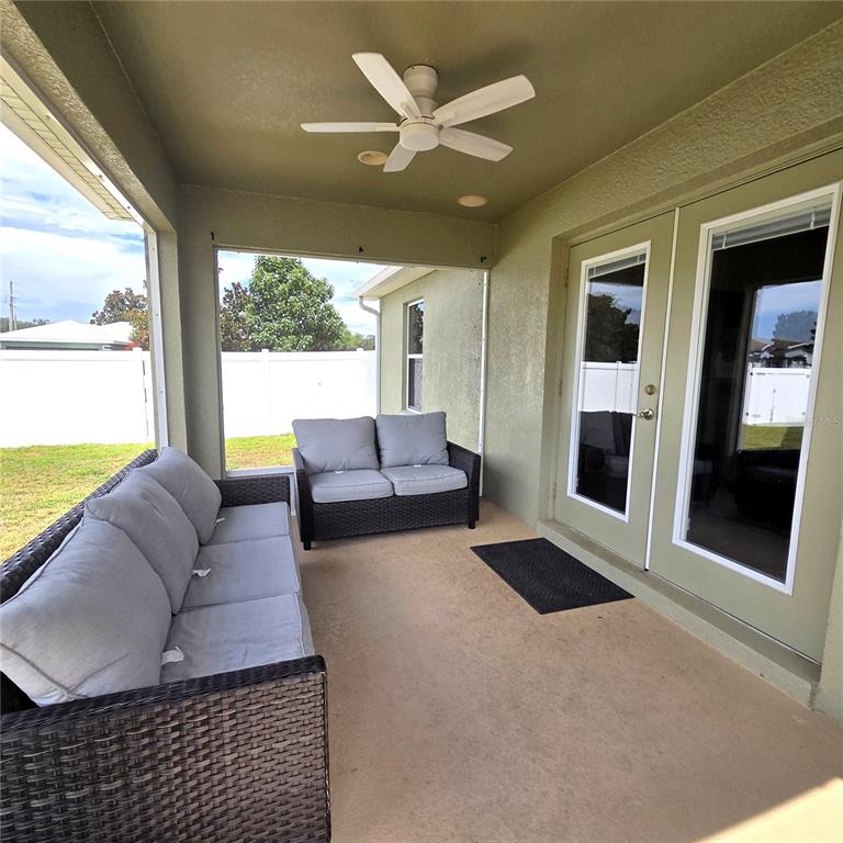 A covered patio features wicker furniture, a ceiling fan, and glass doors leading inside — 2269 COUNTRY MANOR STREET, BARTOW, FL