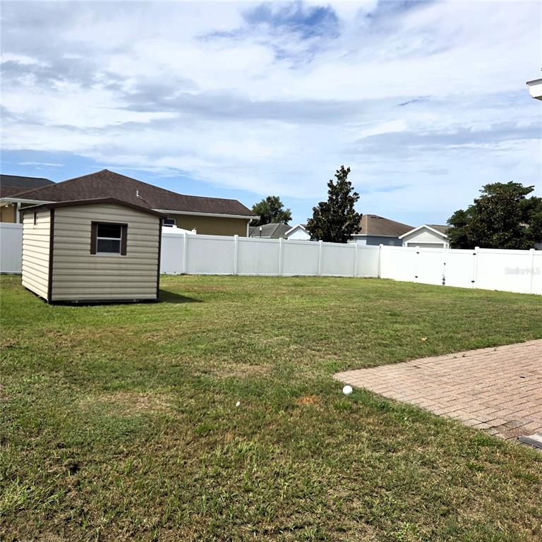 A beige storage shed sits in a grassy backyard enclosed by a white vinyl fence — 2269 COUNTRY MANOR STREET, BARTOW, FL