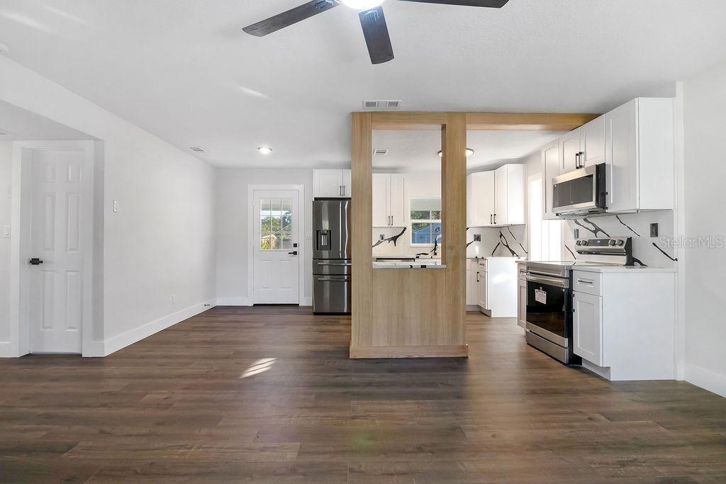 A kitchen with white cabinets and stainless steel appliances opens to a living area — 527 SUNRISE DRIVE, ORLANDO, FL