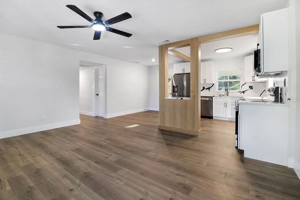 A living room with wood-look flooring opens to a kitchen featuring white cabinets and appliances — 527 SUNRISE DRIVE, ORLANDO, FL
