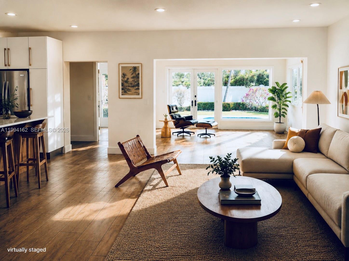 This virtually staged living room features wood floors, a sectional sofa, and a backyard pool view — 3551 E Glencoe St, Miami FL 33133, MIAMI, FL