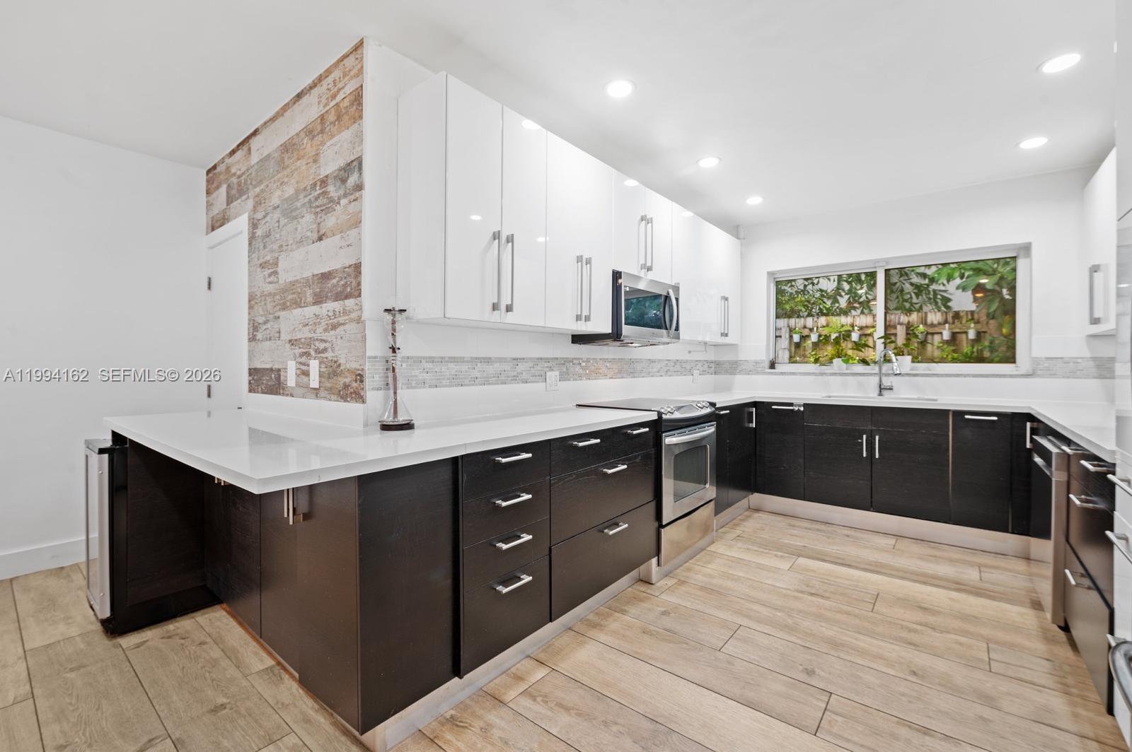 A modern kitchen features white upper cabinets, dark lower cabinets, and wood-look tile flooring — 3551 E Glencoe St, Miami FL 33133, MIAMI, FL