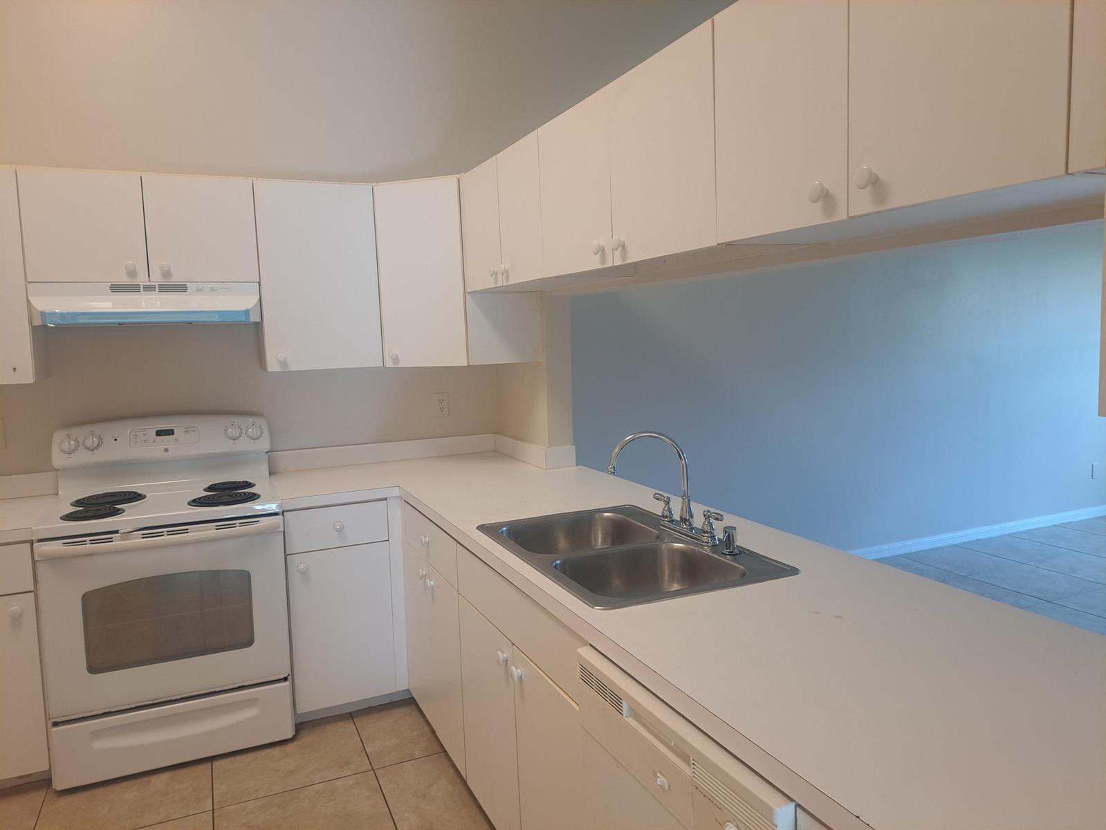 A kitchen features white cabinets, white appliances, a double-basin sink, and light-colored tile flooring — 2838 Stoneway Lane, Fort Pierce FL 34982, FORT PIERCE, FL