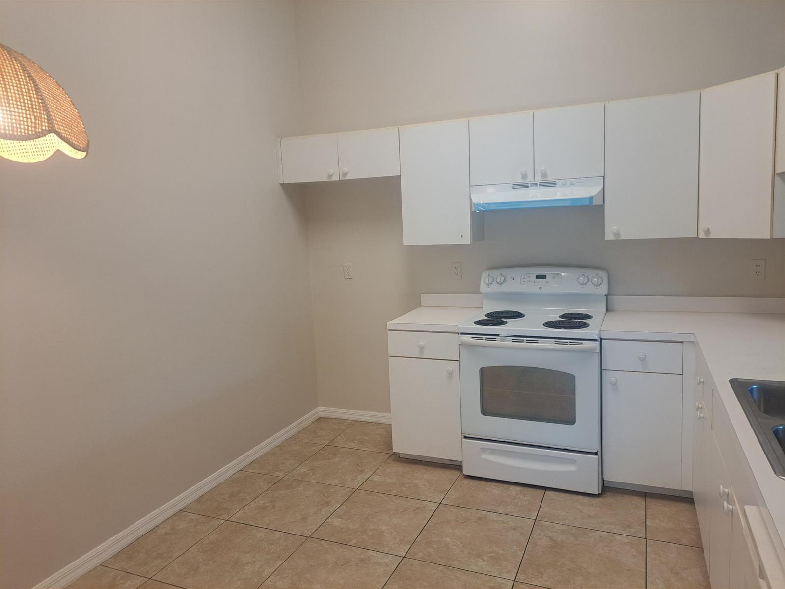 A kitchen features white cabinets, a white electric stove, and tan tile flooring — 2838 Stoneway Lane, Fort Pierce FL 34982, FORT PIERCE, FL