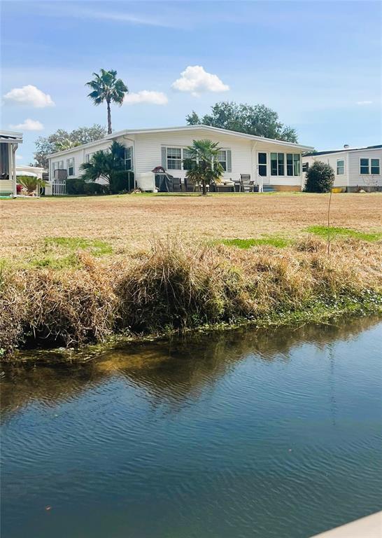 A white single-story house sits behind a grassy lawn and a small canal — 106 PALO VERDE DRIVE, LEESBURG, FL