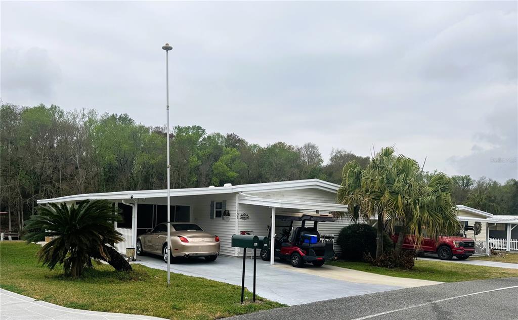 A white mobile home features a carport with a car and a golf cart parked underneath — 106 PALO VERDE DRIVE, LEESBURG, FL