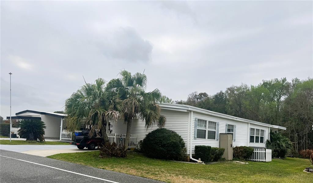 A white manufactured home with a palm tree, carport, and golf cart in the yard — 106 PALO VERDE DRIVE, LEESBURG, FL