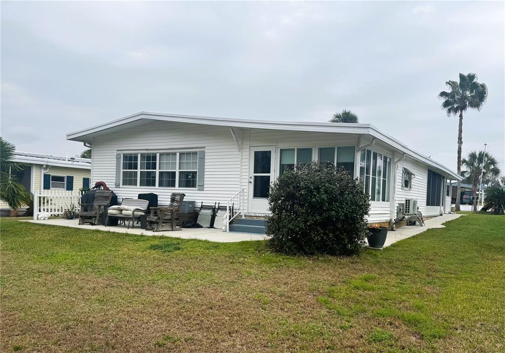 A white single-story manufactured home with a patio and lawn under a cloudy sky — 106 PALO VERDE DRIVE, LEESBURG, FL