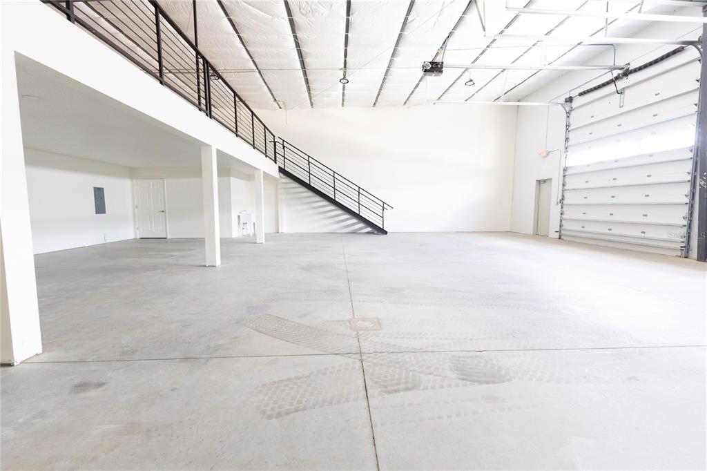 A spacious industrial warehouse interior features a concrete floor, metal staircase, and overhead garage door — 11089 N US HIGHWAY 301 UNIT I-6,I-7, OXFORD, FL