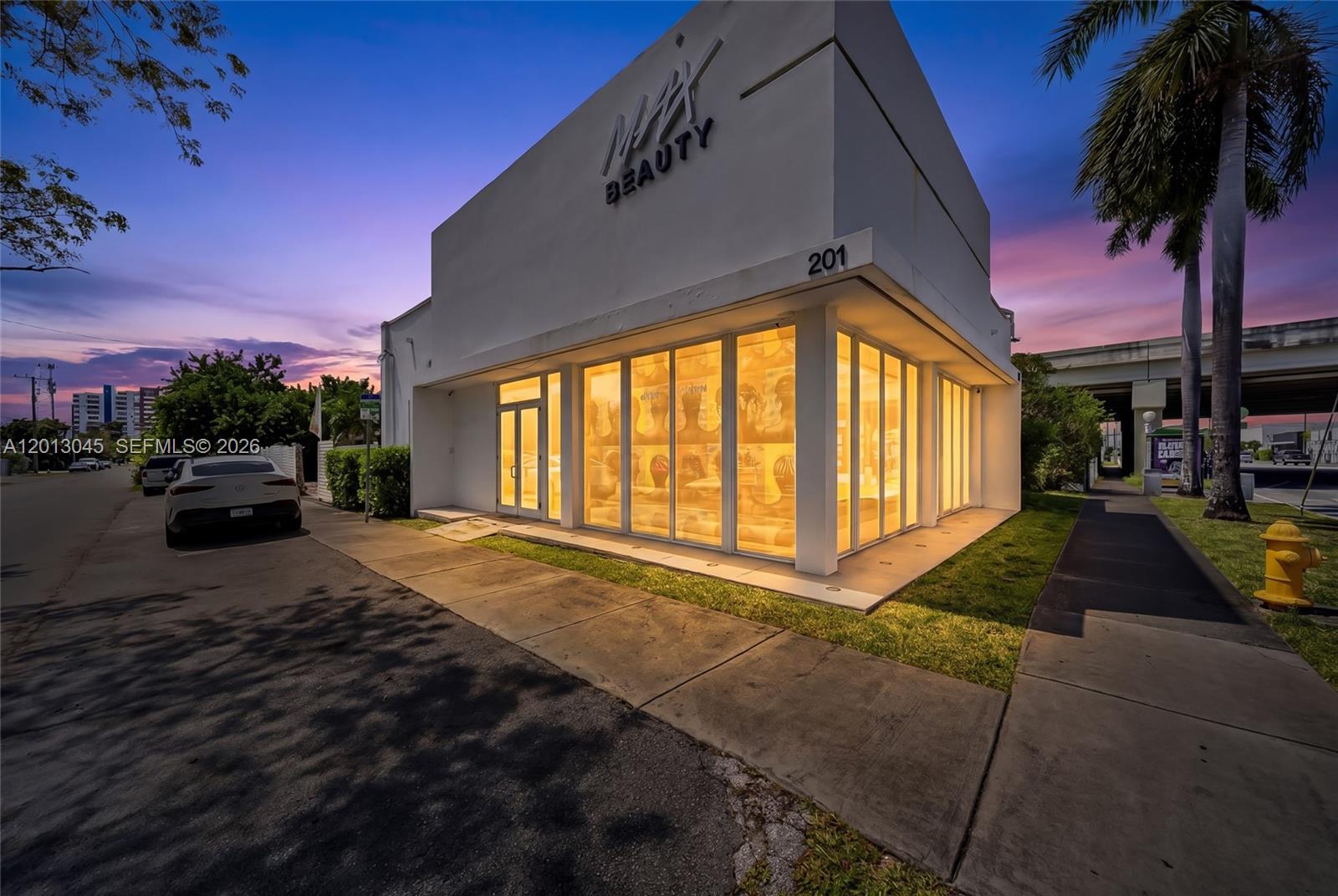 A modern white commercial building with large glass windows at dusk — 201 NW 37th St, Miami FL 33127, MIAMI, FL