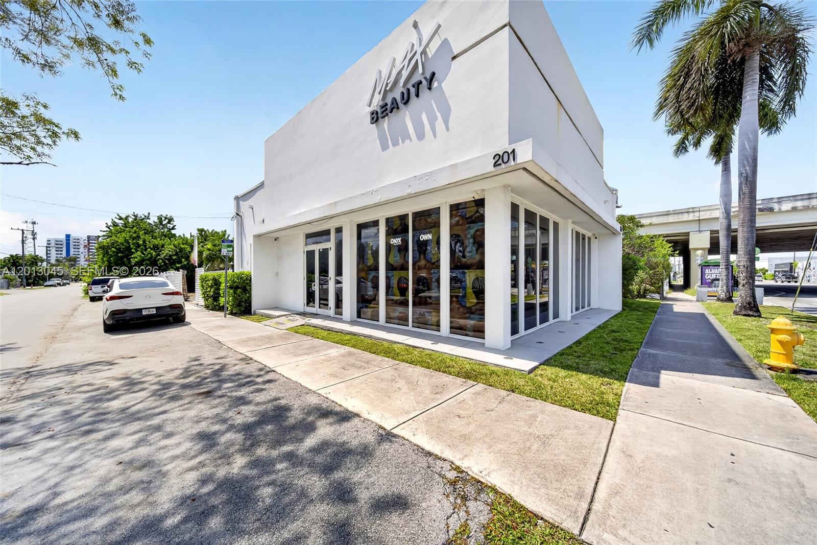 A white commercial building with glass storefront windows and a palm tree on the right — 201 NW 37th St, Miami FL 33127, MIAMI, FL