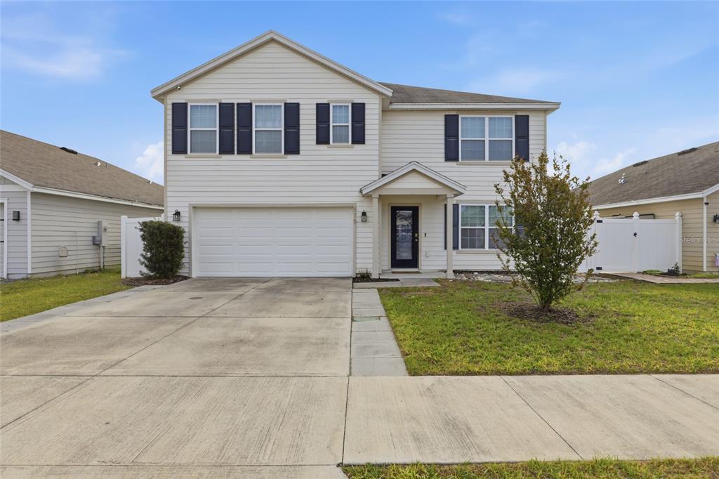 A two-story house with beige siding, a two-car garage, and a front entrance porch — 879 NW 251ST DRIVE, NEWBERRY, FL