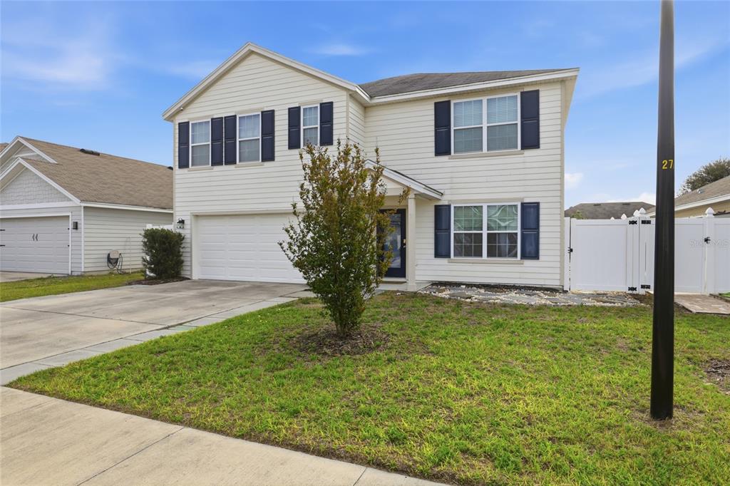 A two-story house with cream siding, dark shutters, a two-car garage, and a front lawn — 879 NW 251ST DRIVE, NEWBERRY, FL