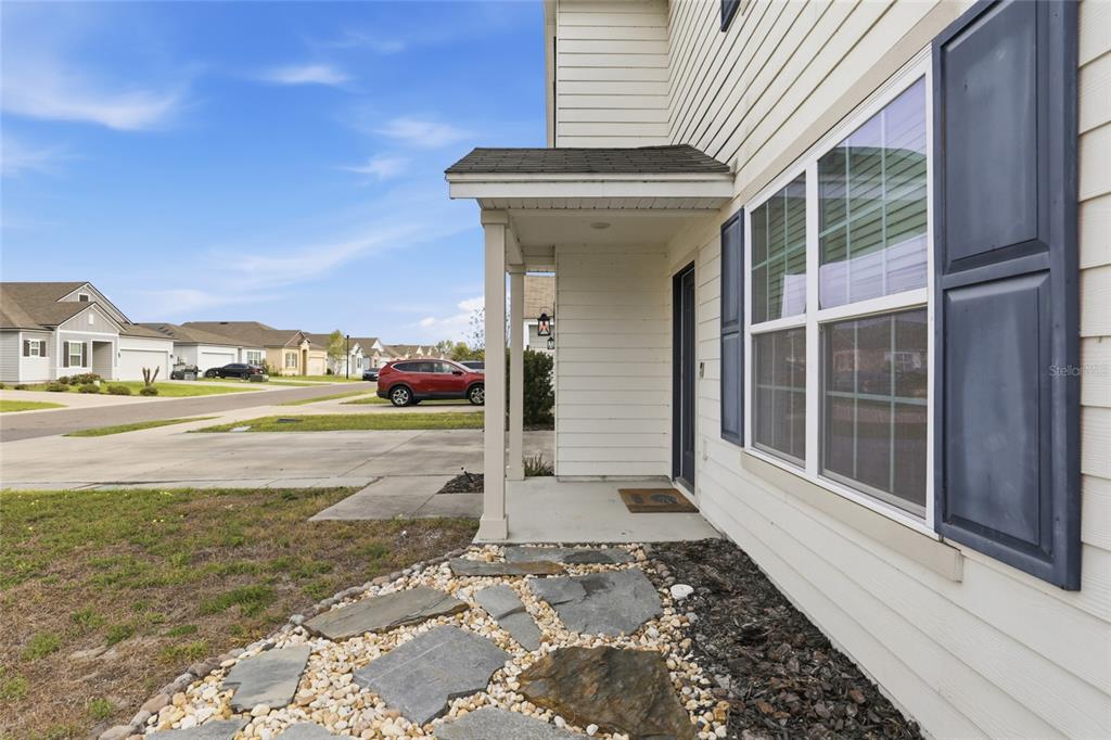 A stone walkway leads to the covered front porch of a beige house with shutters — 879 NW 251ST DRIVE, NEWBERRY, FL