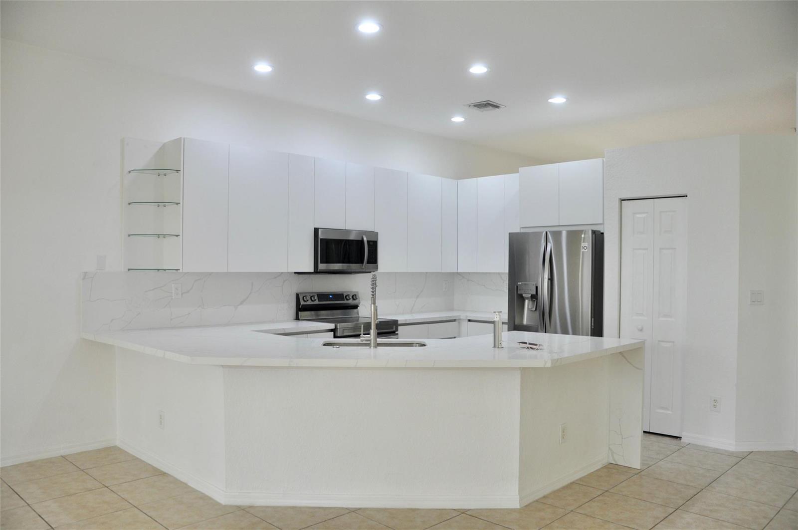 A modern kitchen features white flat-panel cabinets, marble-look countertops, stainless steel appliances, and tile flooring — 19496 S Whitewater Avenue, Weston FL 33332, WESTON, FL