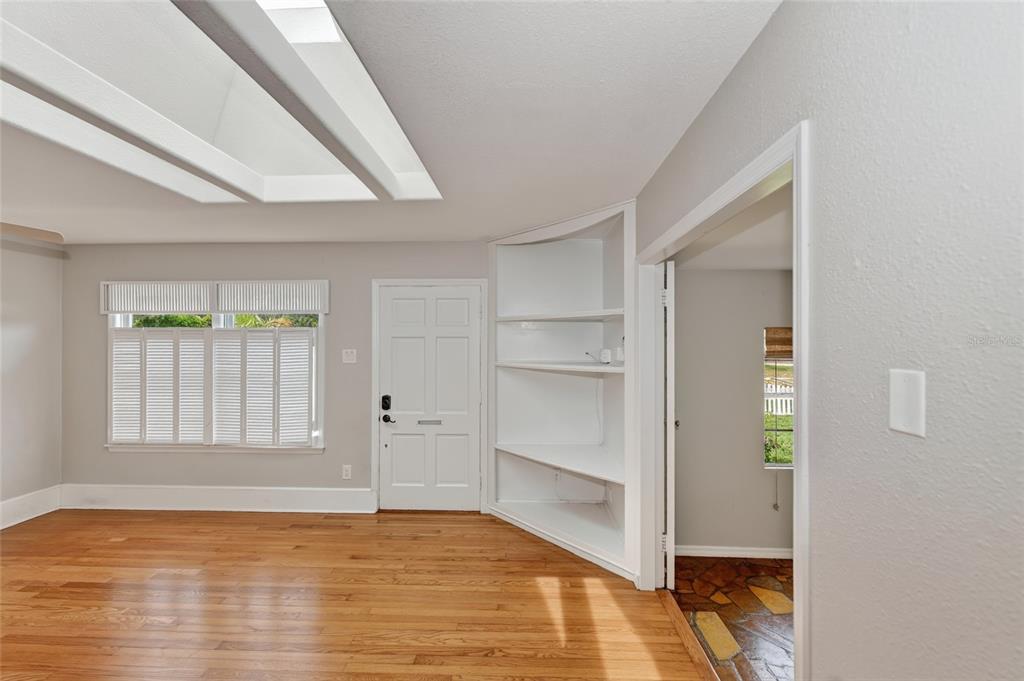 A room with hardwood floors, a white front door, built-in shelving, and a skylight — 1010 VIRGINIA DRIVE, SARASOTA, FL