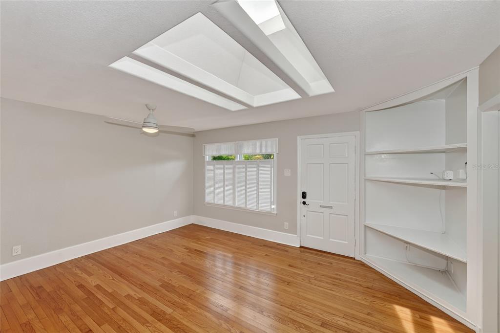 A room with hardwood floors, a ceiling fan, a skylight, a white door, and built-in shelving — 1010 VIRGINIA DRIVE, SARASOTA, FL