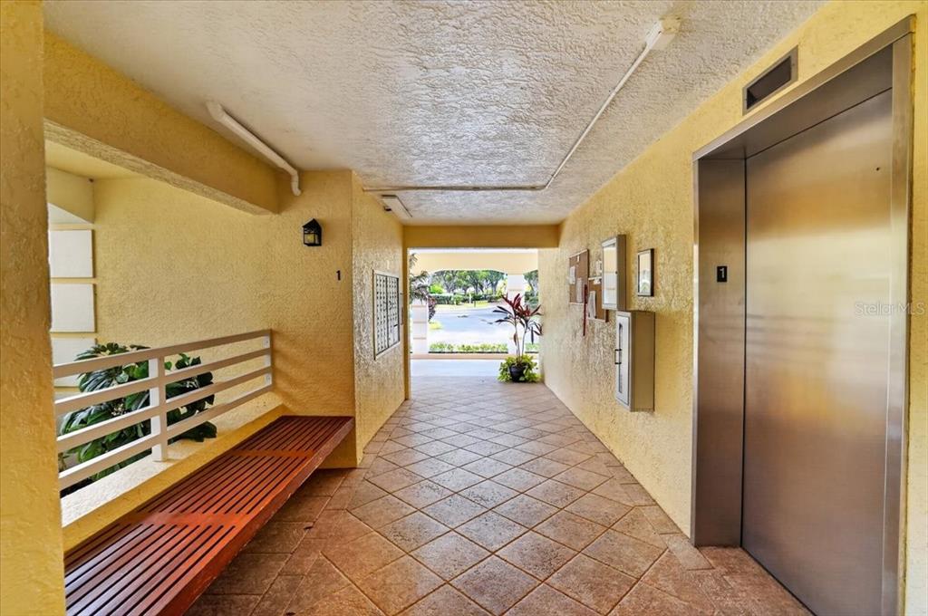 An elevator lobby with tile flooring, a wooden bench, and a view of the outdoors — 1040 WEXFORD BOULEVARD UNIT 1040, VENICE, FL
