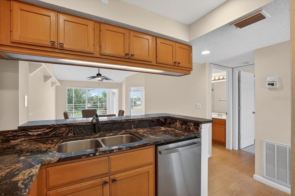 A kitchen features wood cabinets, dark granite countertops, a stainless steel dishwasher, and a sink — 1040 WEXFORD BOULEVARD UNIT 1040, VENICE, FL