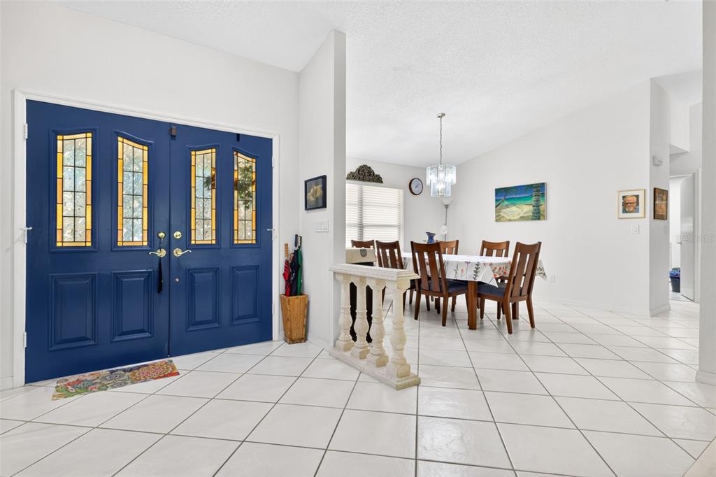 A bright entryway with white tile floors leads to a dining area with a blue door — 5035 BARROWE DRIVE, TAMPA, FL
