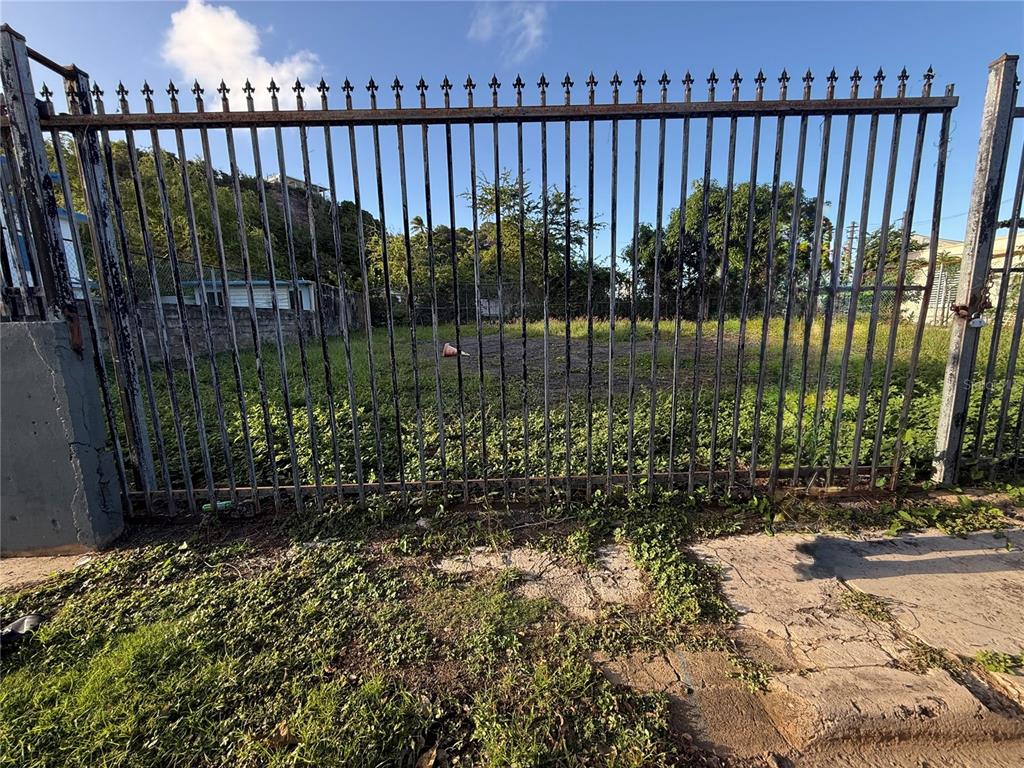 A metal gate stands in front of an overgrown, fenced-in vacant lot — . UNION UNIT 475, PUERTO REAL, PR