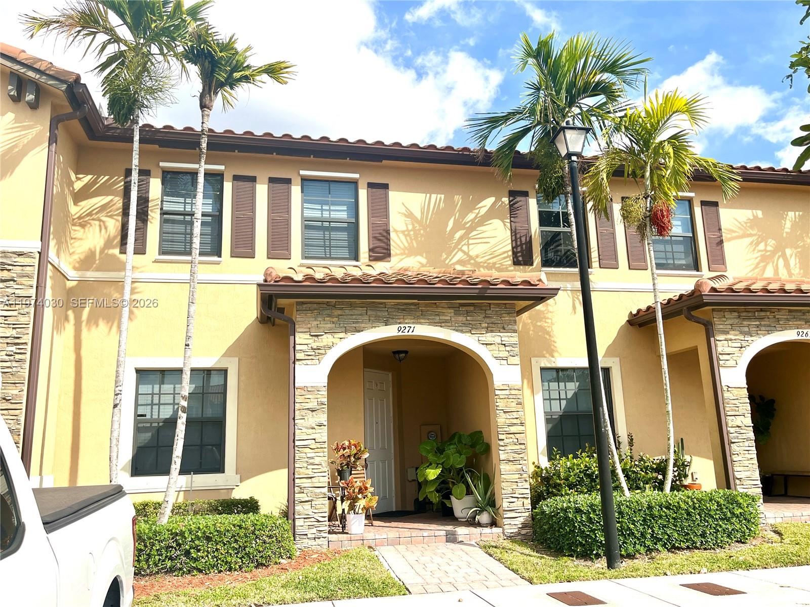A two-story tan stucco townhouse features a stone-accented entryway and palm trees in front — 9271 W 33rd Ln, Hialeah FL 33018, HIALEAH, FL