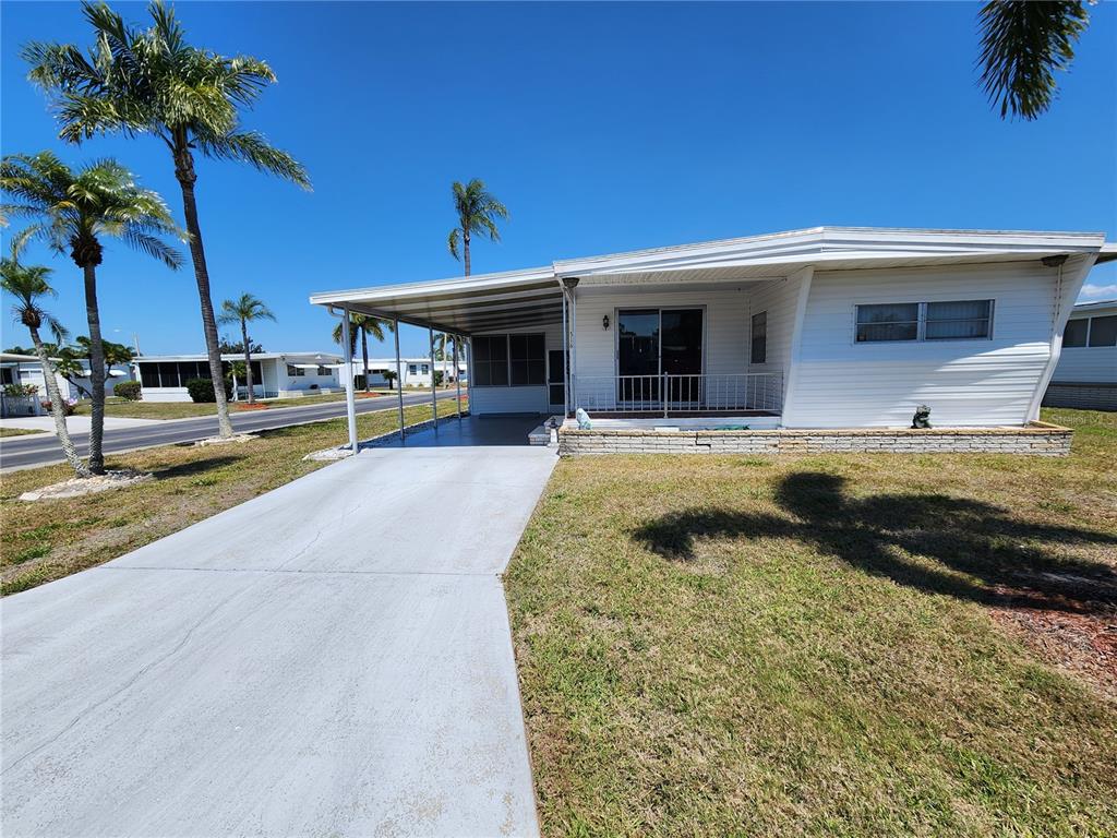 A single-story mobile home with a carport, front porch, and palm trees on a lawn — 316 DANUBE CIRCLE, BRADENTON, FL