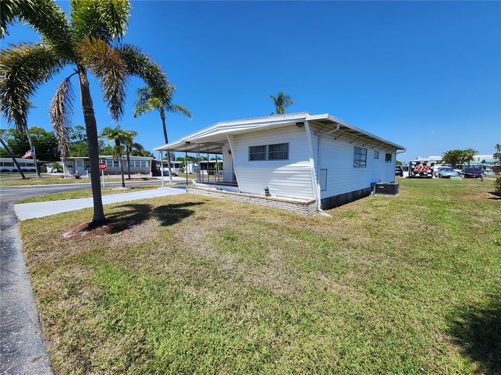 A white mobile home with a covered porch sits on a grassy lot with palm trees — 316 DANUBE CIRCLE, BRADENTON, FL