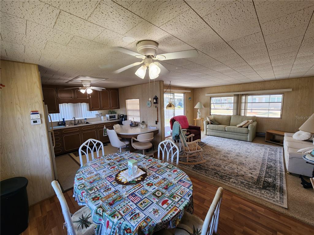 An open-concept living and dining area features wood-paneled walls, a drop ceiling, and laminate flooring — 316 DANUBE CIRCLE, BRADENTON, FL