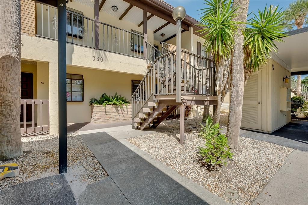 An exterior view of a two-story apartment building with a wooden staircase and gravel landscaping — 360 THREE LAKES LANE UNIT E, VENICE, FL