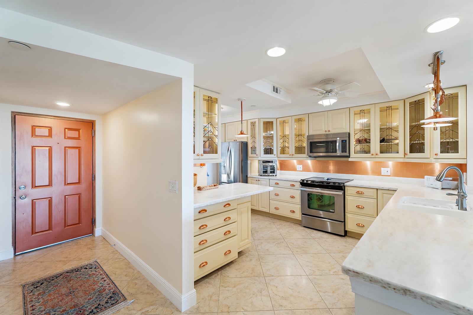 A kitchen features cream-colored cabinets, stainless steel appliances, copper-toned backsplash, and a marble-topped island — 356 Golfview Road # 903, North Palm Beach FL 33408, NORTH PALM BEACH, FL
