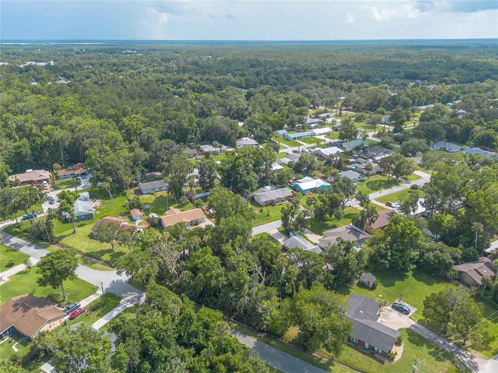 An aerial view shows a residential neighborhood with houses surrounded by dense trees and greenery — 2433 CLAIRE AVENUE, NEW SMYRNA BEACH, FL