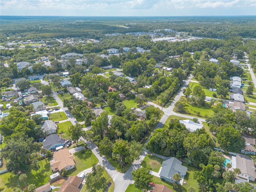 An aerial view shows a suburban neighborhood with houses, dense trees, and paved streets — 2433 CLAIRE AVENUE, NEW SMYRNA BEACH, FL