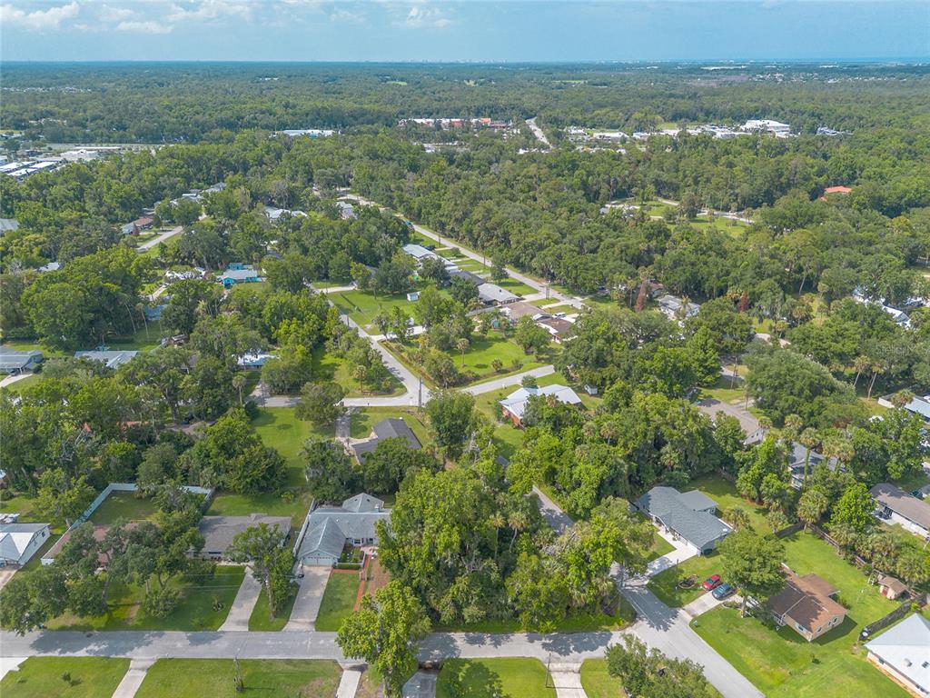An aerial view shows a residential neighborhood with houses surrounded by dense green trees — 2433 CLAIRE AVENUE, NEW SMYRNA BEACH, FL