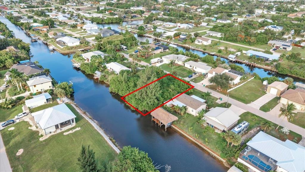 An aerial view shows a vacant, tree-covered residential lot outlined in red along a canal — 3631 MAGNOLIA WAY, PUNTA GORDA, FL