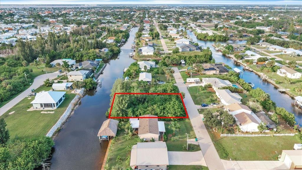 An aerial view shows a rectangular, tree-covered vacant lot situated between a canal and road — 3631 MAGNOLIA WAY, PUNTA GORDA, FL