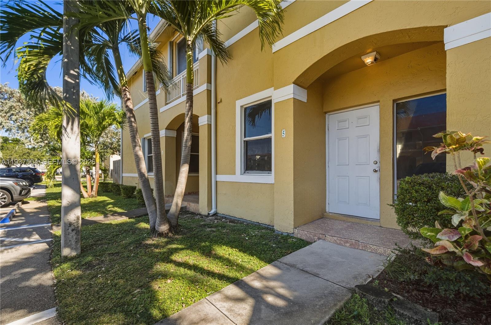 A yellow two-story building with a white front door and palm trees in the yard — 810 NE 212th Ter # 5, Miami FL 33179, MIAMI, FL