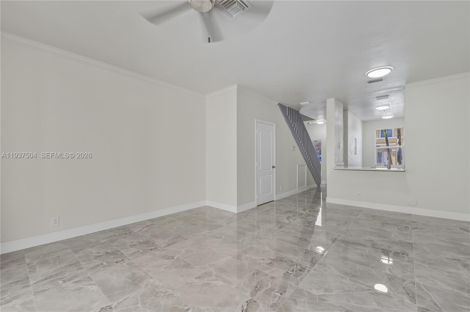 An empty living room features glossy marble-look tile flooring, white walls, and a staircase — 810 NE 212th Ter # 5, Miami FL 33179, MIAMI, FL