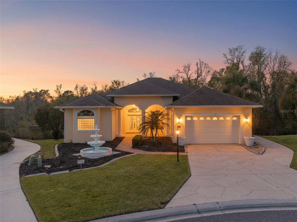 A single-story house with a fountain, a paved driveway, and a two-car garage at sunset — 6410 BENDELOW DRIVE, LAKELAND, FL
