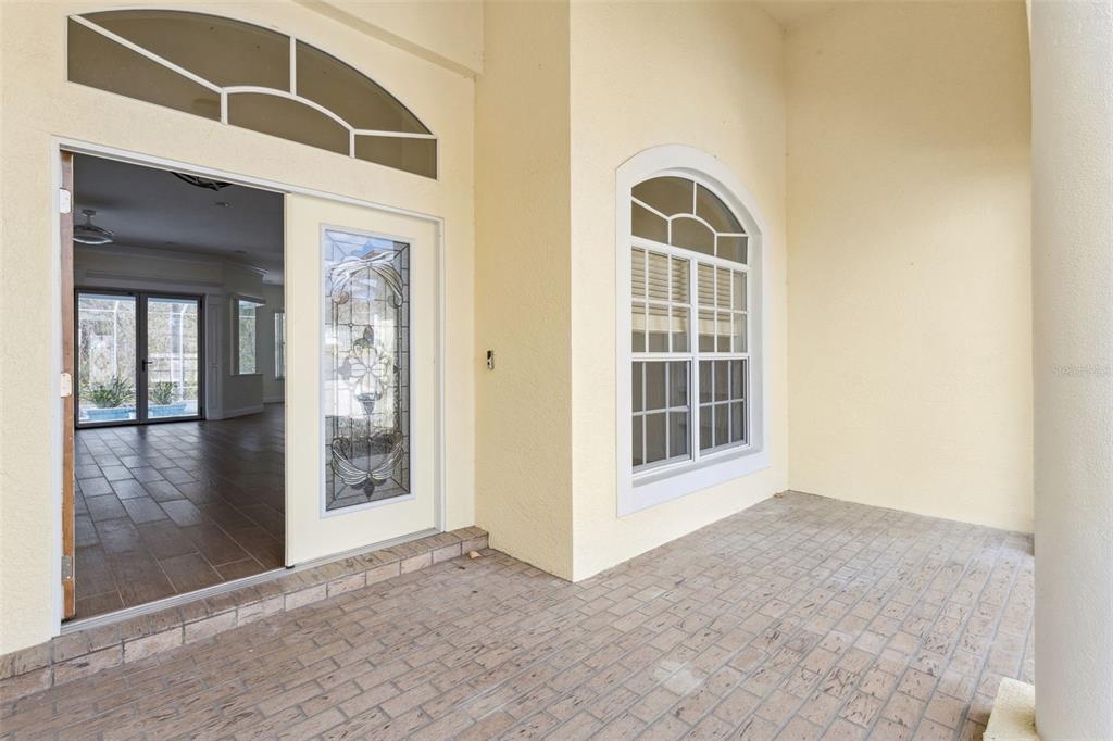 A covered entryway features a brick-paver floor, a decorative glass front door, and arched windows — 6410 BENDELOW DRIVE, LAKELAND, FL